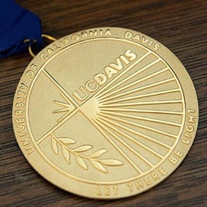 Gold UC Davis Medal on a wooden grain surface.
