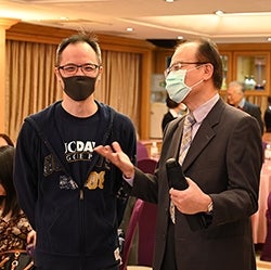 Two alumni standing and speaking at an indoor event wearing face masks.