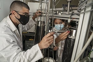 Man and woman in lab coats working on machinery.