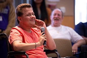 Man smiling is sitting in a chair with a microphone close to his mouth.