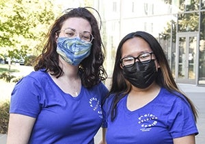 Two girls with glasses, masks, and blue shirts that say "Aggies helping Aggies"