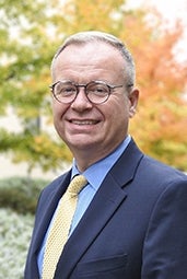 Older man with glasses, in suit, smiling.