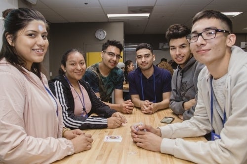 Six students sitting around a table smiling at camera