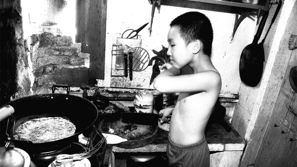 Black and white photo of Martin Yan, at age 9, as he cooks in his family's kitchen in China.