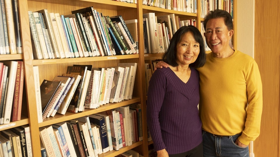 Chef Martin Yan and his wife, Susan, standing in front of a bookshelf smiling.