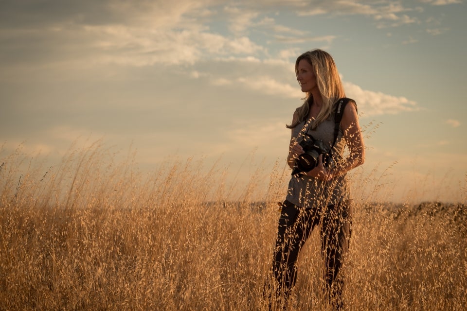 Jackie Anderson holding a camera while standing in a field and looking out at the horizon