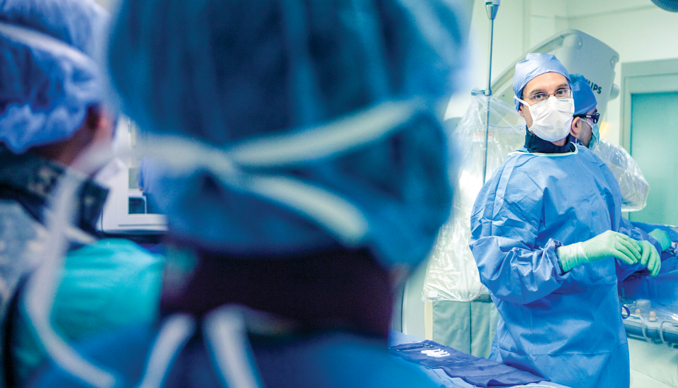 Jeff Southard wears blue scrubs, surgical cap, gloves, and a mask in a surgical suite.