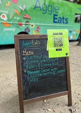 An A-frame chalkboard with AggieEats menu and QR code.