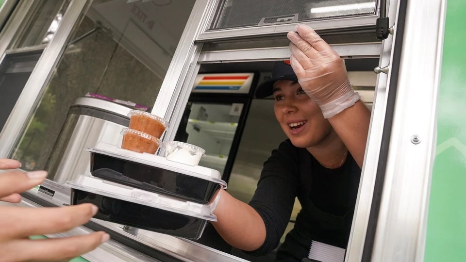 Bianca Tomat, a second-year student studying food science, serves two meals through the window of the AggieEats food truck.