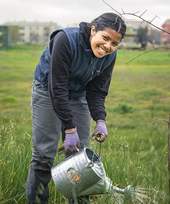 Nurjannah Wiryadimejo wears purple gloves and waters trees with a silver watering can.