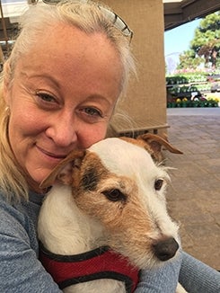Isabelle Alessandra holding her Russell Terrier close to her face and smiling. The dog is wearing a red harness.