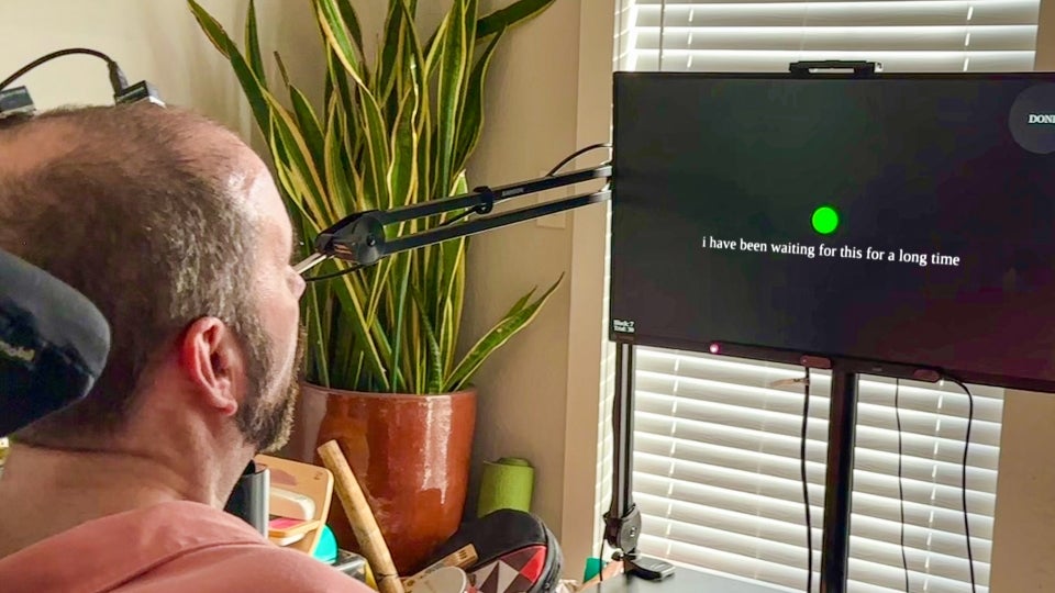 A study participant with ALS uses a brain–computer interface to communicate. As he attempts to speak, a brain implant records neural signals that are decoded into words on a screen. The text on the screen reads "I have been waiting for this for a long time."