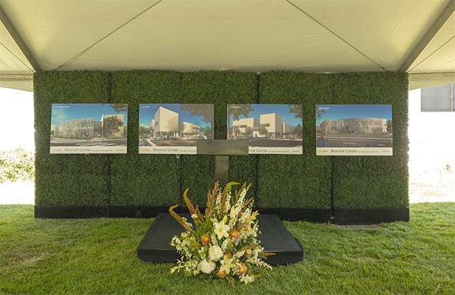 Renderings of the Lynda and Stewart Resnick Center for Agricultural Innovation on a grassy backdrop in front of a short podium with a large flower arrangement in front.