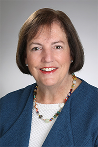 Deb Neff's headshot wearing a blue blazer and white top with a statement necklace in front of a grey backdrop.