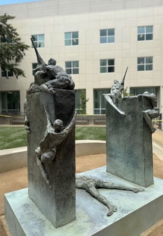 A sculpture of two walls with people climbing them in the courtyard of the library.