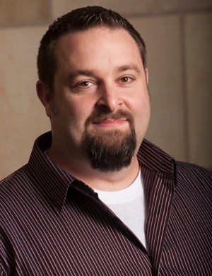 Associate Professor John Gray wearing a striped maroon button-down shirt.