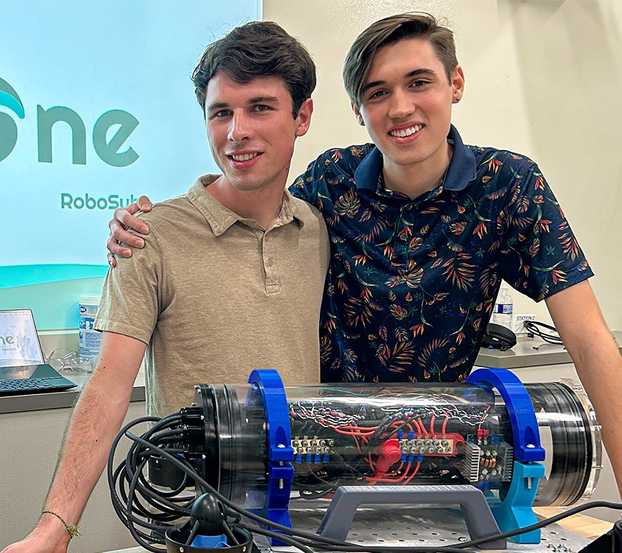 Co-founders of Cyclone RoboSub pose with a small submarine that operates without a human controlling it.