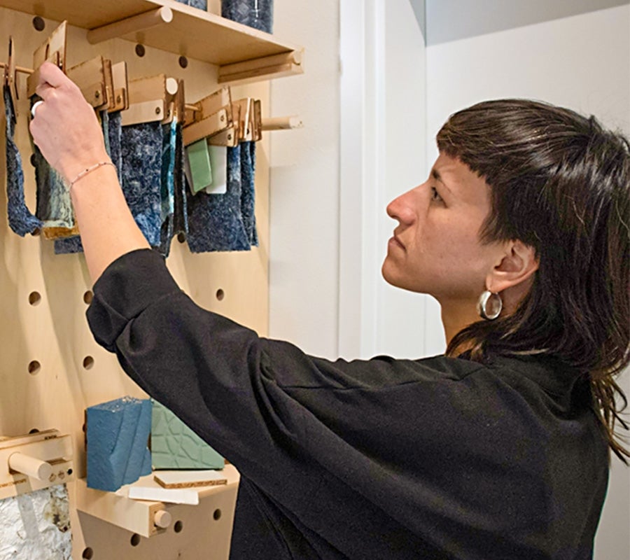 Alejandra Ruiz inspects fabric samples hanging from a pegboard.