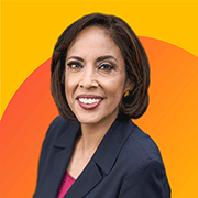 An image with a bright yellow background. A photograph of Anna Maria Chavez is displayed, smiling and dressed in a black blazer. A soft orange semicircle decorates the background.