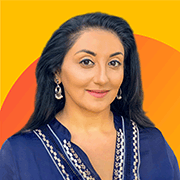 An image with a bright yellow background. A photograph of Amishi Jha is displayed, smiling and dressed in a dark blue top with a pattern trim. A soft orange semicircle decorates the background.