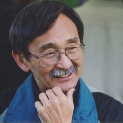 Dr. Isao Fujimoto wearing glasses smiling while resting one hand under the chin.