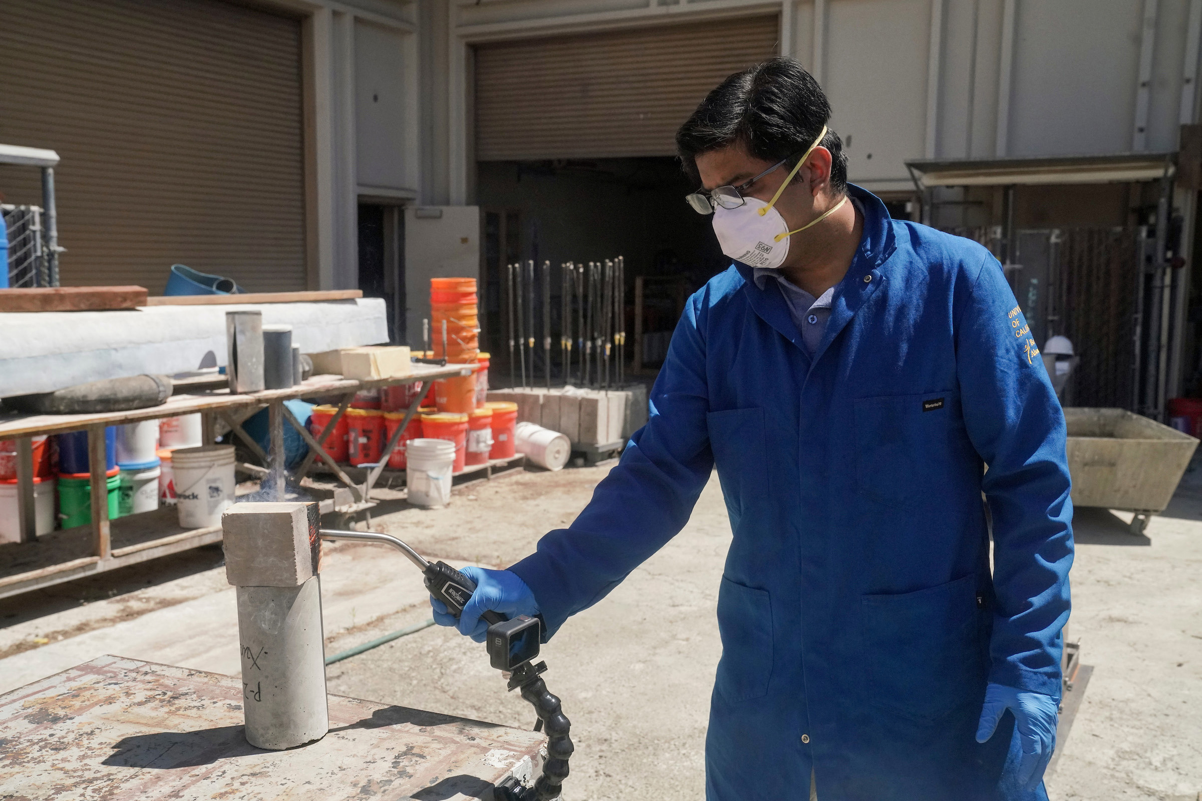 Person holding blow torch, using it on a lab-made earth block outdoors.