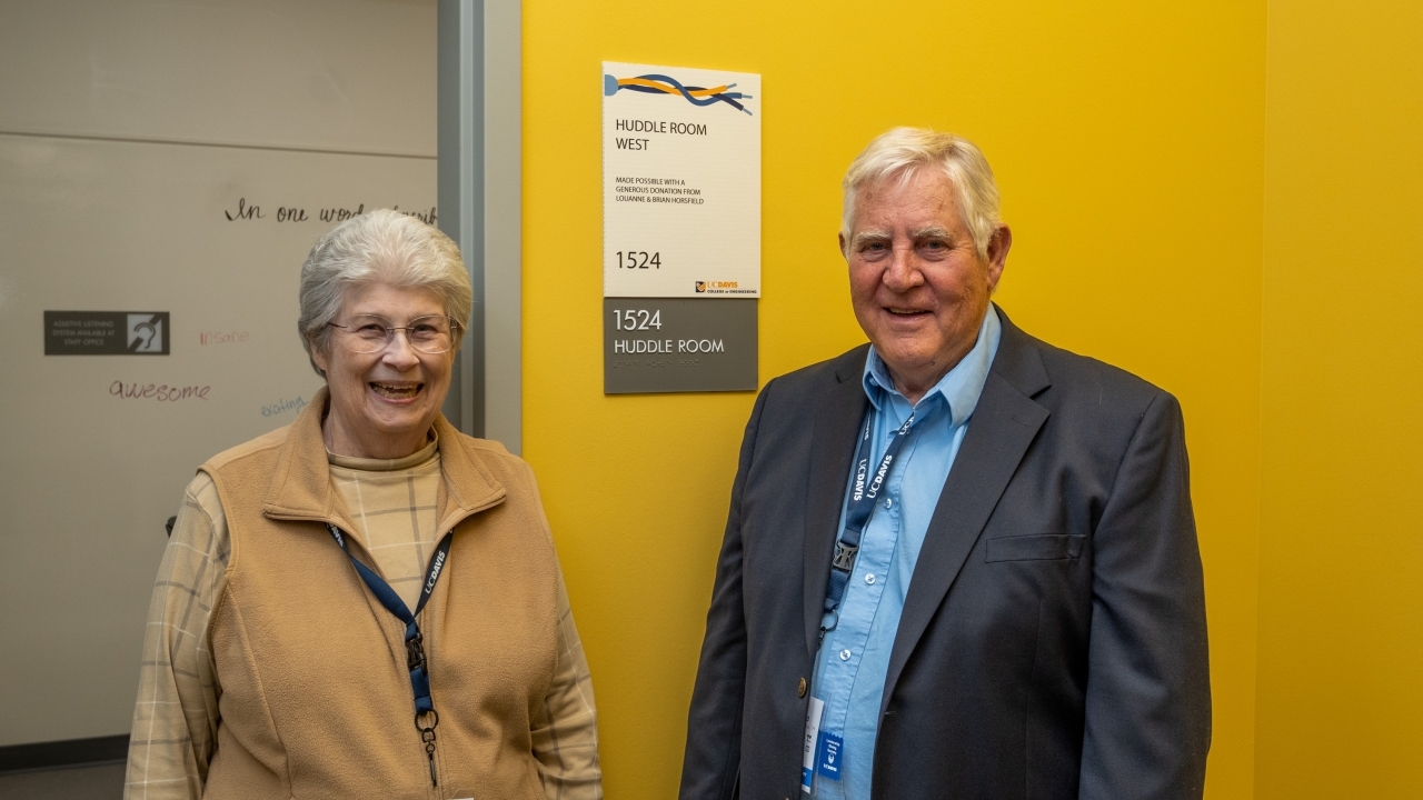 Brian Horsfield and wife Louanne Horsfield in front of a named room with a sign titled "Huddle Room West" in the UC Davis College of Engineering.
