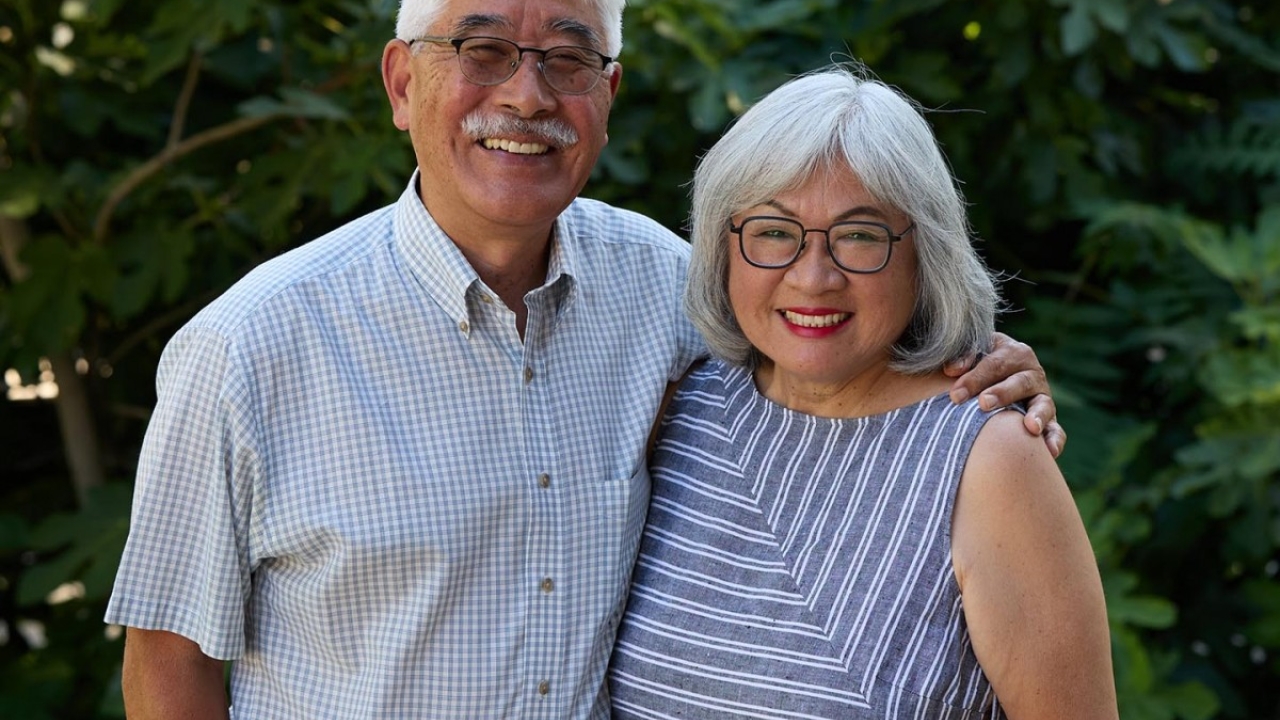 Gary and Sharon Takahashi pose outdoors in front of greenery.
