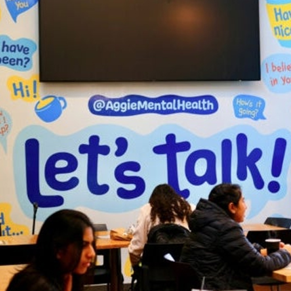 Students studying at the Coffee House with a large mural with encouraging phrases such as "Let's talk!" and "Have a nice day"
