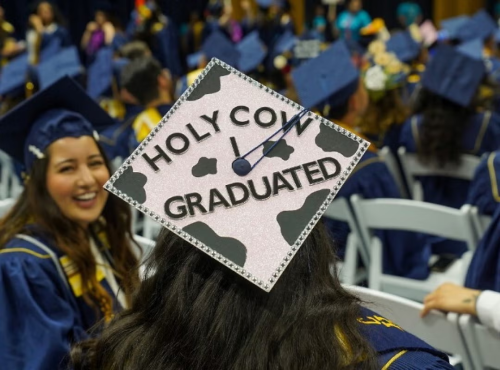 A decorated grad cap that reads "Holy cow I graduated."