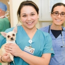 A student holding a dog with another student in the background