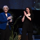 Sue Ebeler poses with a glass award on stage next to Kelly Brown.