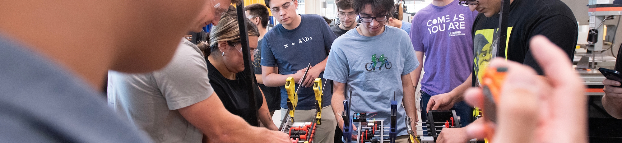 A group of engineering students gather around a workstation with gadgets, clamps and hydraulics.